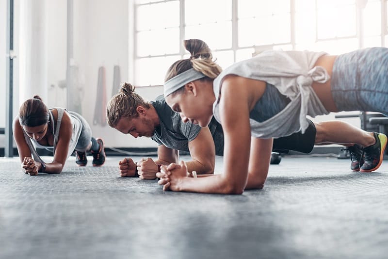 Three people are performing plank exercises on a gym floor.